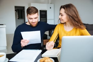 Two people at a laptop reviewing paperwork and smiling
