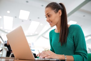 Woman in green sweater looking at a laptop screen.