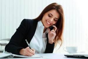 Woman speaking into a phone while taking notes.