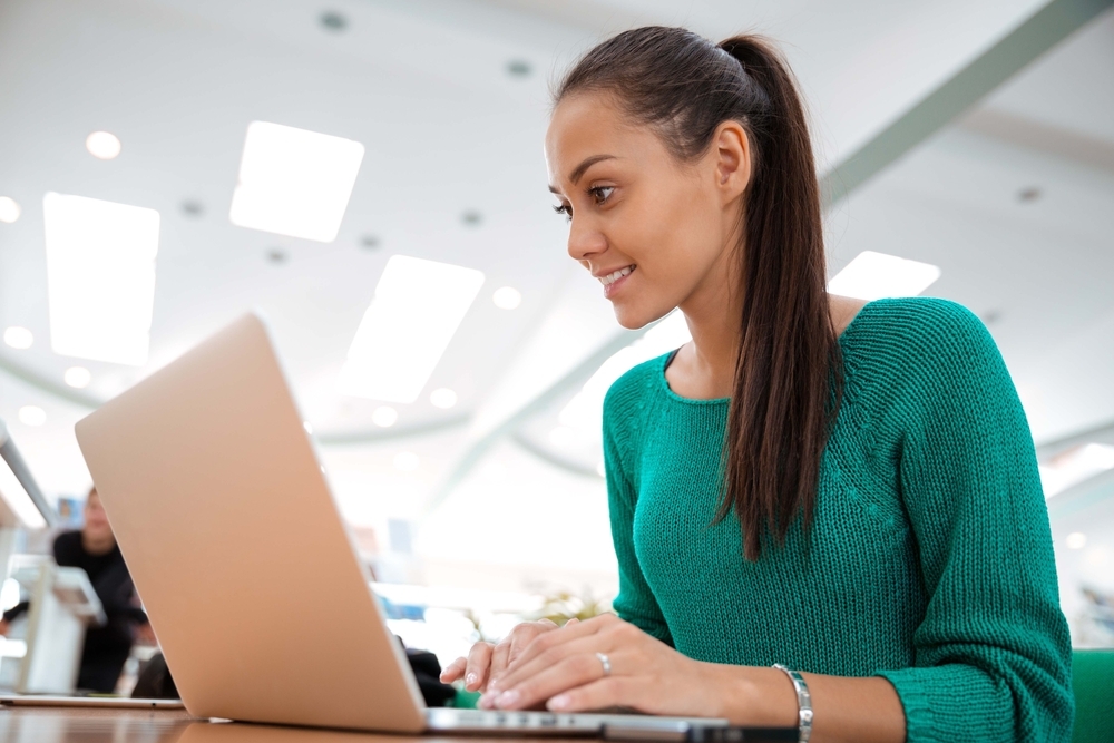 Woman in green sweater looking at a laptop screen.